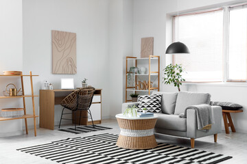 Interior of stylish living room with grey sofa, coffee table, workplace and shelving unit