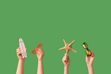 Female hands with stylish sunglasses, starfish and mini surfboard on green background