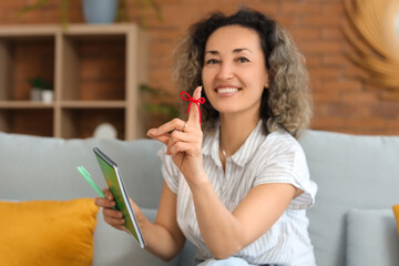 Beautiful middle-aged woman with red string on her finger and notebook trying to remember something...