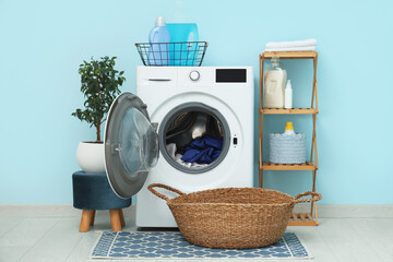 Modern washing machine with rack, basket and detergents near blue wall