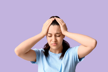 Young woman suffering from headache on lilac background