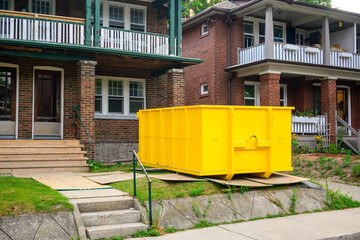 A roll-off construction dumpster bright yellow outside a residential renovation project in an older neighourhood. shot in toronto in the summer.	
