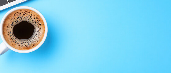 Cup of black coffee with foam on blue background next to laptop keyboard, creating calm and productive workspace