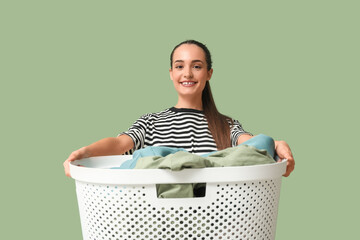 Beautiful young happy woman with basket of clean laundry on green background