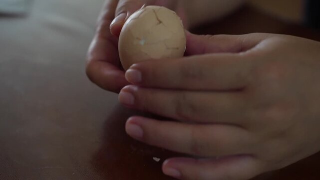 Close up of woman cracking egg shell on table then peeling shell from boiled egg