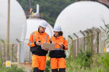 Engineers Working at Industrial Plant with Storage Fuel Tanks, Two Industrial Workers with Laptop and Walkie-Talkie Outdoors, Male and Female Technicians Inspecting Facility