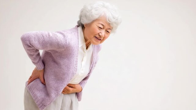 七十五歳の日本人の高齢女性が静かに腰を押さえる