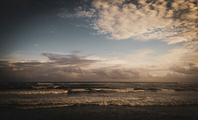 Golden light brushes the clouds and sea as soft waves roll under a serene sky. A peaceful seascape...