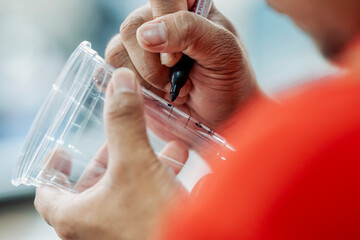 Close-up of a barista using a marker to write a customer's name on a clear plastic coffee cup for...