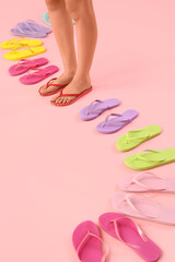 Female legs with colorful flip-flops on pink background
