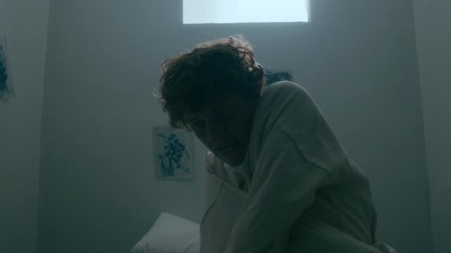 Young man with mental disorder struggling to escape straitjacket in white room with flickering light at psychiatric hospital