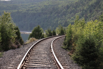 Fototapeta premium Railway in the countryside of Charlevoix in Quebec and in Canada. Summer landscape and horizon. Travel and destination and train transportation. Summer calendar with a view of a riverside.
