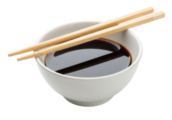 A white bowl filled with dark soy sauce with wooden chopsticks resting on top isolated on white background