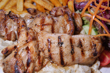 Grilled chicken with fries and fresh salad at a dining table
