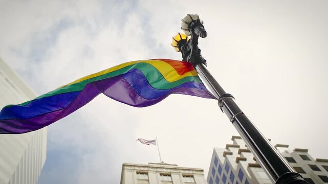 A rainbow pride flag waves in the wind next to a vintage street lamp in  San Francisco, California, USA. The flag represents LGBTQ+ pride and equality.