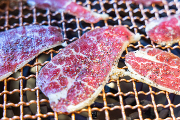 Sliced raw beef being grilled on a metal grid