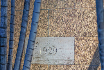 White Cornerstone, Circa 1929, on a Tan Building with Stalks of Bamboo in the Foreground.
