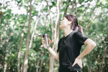 Young woman taking a break and drinking water in the forest