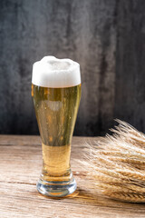 A glass of beer with foam and wheat ears on wooden table
