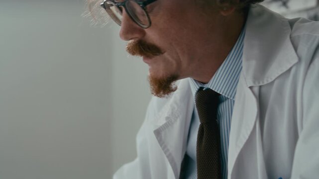 Male doctor in white coat taking notes on paper and speaking during clinical session in psychiatric hospital ward. Close-up, tilt-up shot