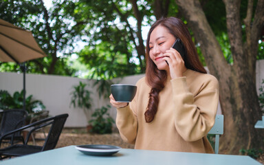 Portrait image of a young woman talking on mobile phone while drinking coffee in the outdoors cafe