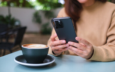 Closeup image of a woman holding and using mobile phone with coffee cup on the table