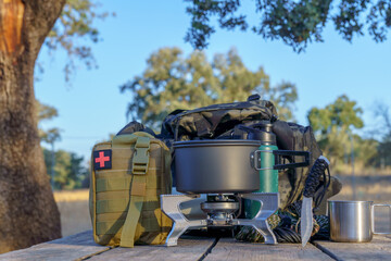 Essential camping gear, including a cooking pot, portable stove, first aid kit, and backpack, sits...