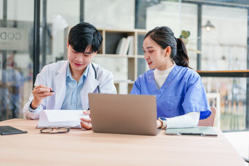 Two medical professionals discussing patient information with laptop and documents in modern office, showing focused and collaborative atmosphere