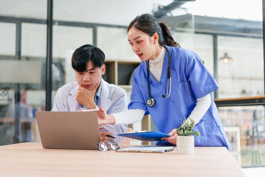 Medical team working together in modern office, focused doctor and nurse discussing patient data on laptop with clipboard, healthcare collaboration and teamwork concept