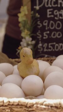 A basket of fresh eggs for sale at a farmer's market in the Ferry Building, San Francisco, California, USA. A small duck figurine sits atop the eggs, adding a touch of whimsy to the display.