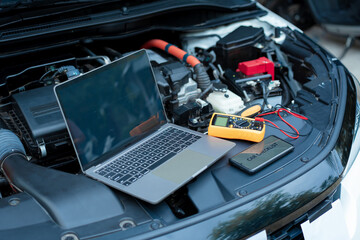 Essential car maintenance tools set up: a laptop rests on the open engine bay, a smartphone...