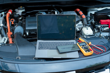 Essential car maintenance tools set up: a laptop rests on the open engine bay, a smartphone...
