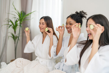 Diverse group of beauty women enjoy skincare routine, applying cucumber eye masks for hydration and...