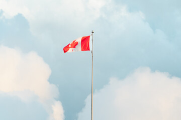 Canada’s national flag fluttering in the wind under a partly cloudy sky.