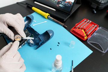 Gloved hands holding vibration motor of a video game controller during a repair with tools on desk