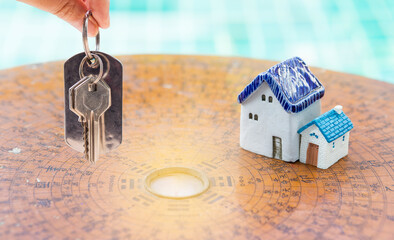 House key in girl hand with miniature house on wooden chinease compass, outdoor day light, property...