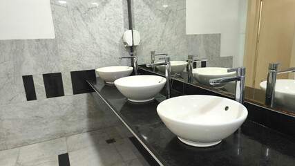 Modern white ceramic sinks with chrome faucets on a black countertop in a clean public restroom,...