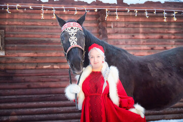 Beautiful Russian girl in national dress poses with a horse during Maslenitsa celebration in winter