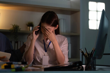 Stress and Overwhelm. Young woman on phone, feeling stressed at work in a dimly lit office.