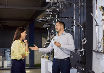 Cheerful salesman having fun while talking with woman customer, holding shower head, recommending...