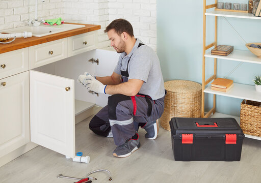 Plumber man, professional worker changes pipes under sink, fits and repairs fittings, water supply, sanitation, heating systems plumbing, sewage, installations, garbage disposal repair, drain cleaning