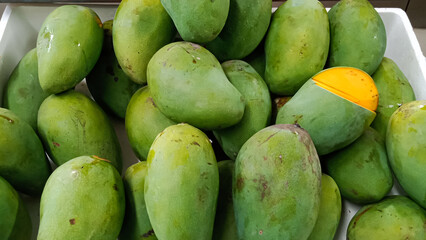 A vibrant pile of fresh green mangoes, with one peeled to reveal its golden flesh.