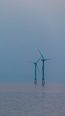 Offshore wind turbines visible above the sea filled with mist.