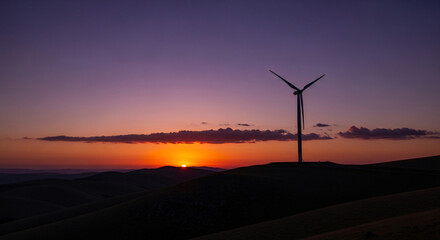 Obraz premium Silhouette of a Wind Turbine Against a Sunset Sky Generating Power.