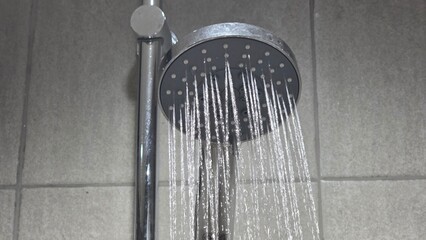 Modern chrome shower head releasing water in straight streams, mounted on tiled wall, showing...