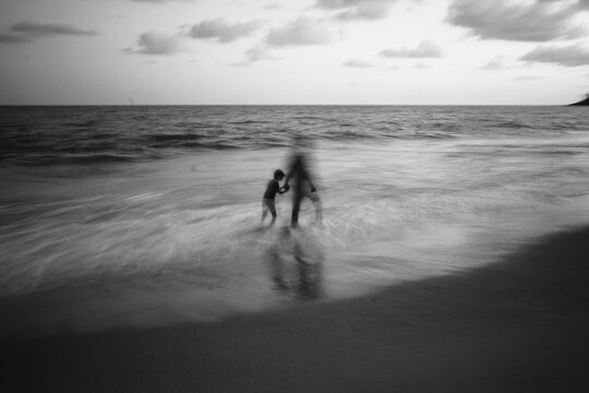 Blurred artistic monochromatic image of father and son walking in a beach - Powered by Adobe