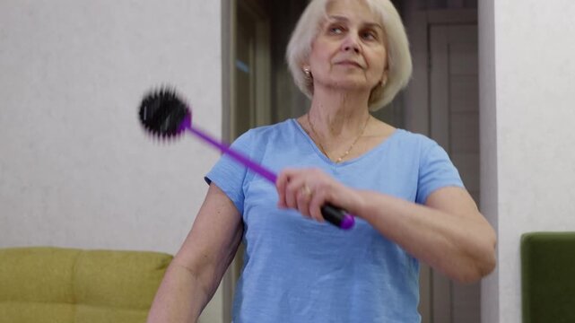 Senior woman leveraging roller massager for tapping targeted muscle tension relief, supporting wellness and maintaining active lifestyle during aging process at home setting