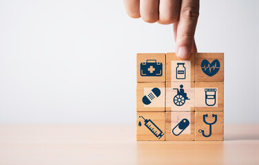 A hand is placing a wooden block on a stack of blocks, each depicting healthcare symbols like a...
