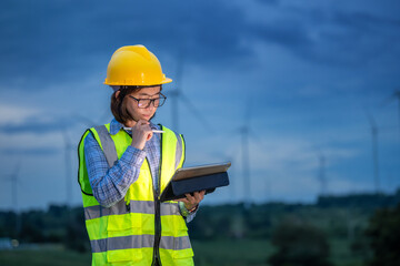 A woman in a yellow safety vest is writing on a clipboard in front of a wind farm. Concept of...
