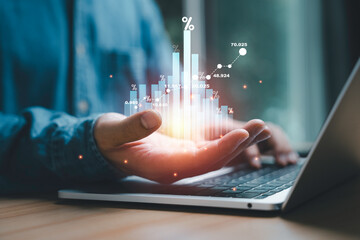 Gesturing toward a glowing bar graph overlaying a laptop. The graph represents data analytics,...